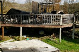 charred remains of a house, with a deck railing in front