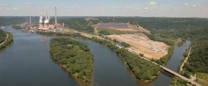 In an aerial view, a power plant with large smokestackes can be seen along a large river.