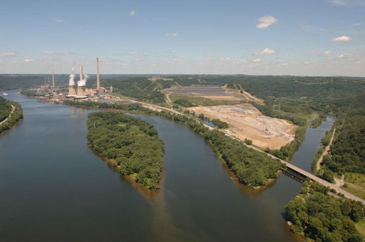 In an aerial view, a power plant with large smokestackes can be seen along a large river.