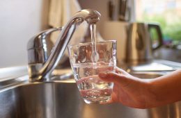 A hand holds a glass in a kitchen sink that is being filled with water