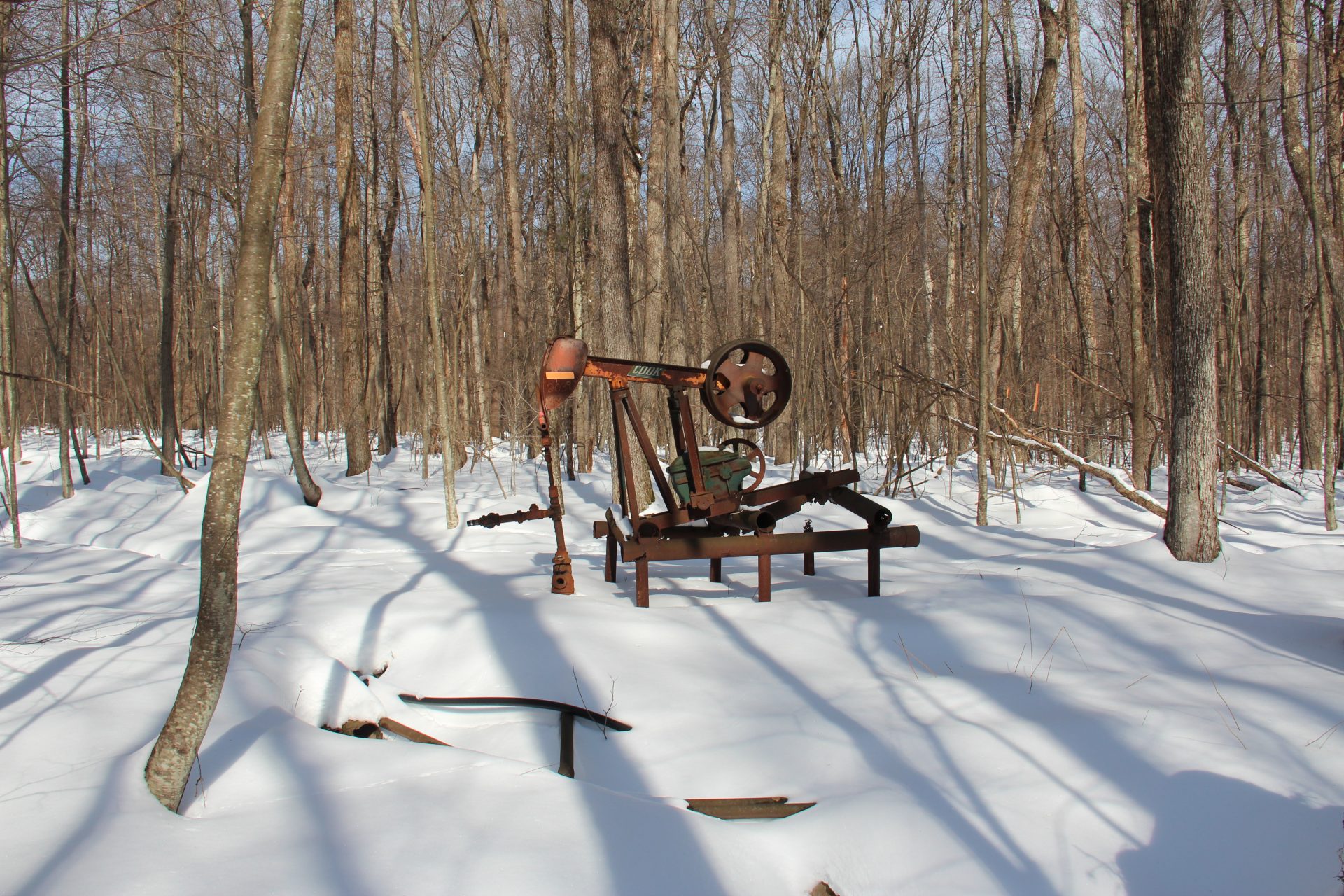 An rusty, abandoned oil well in a snow-covered forest
