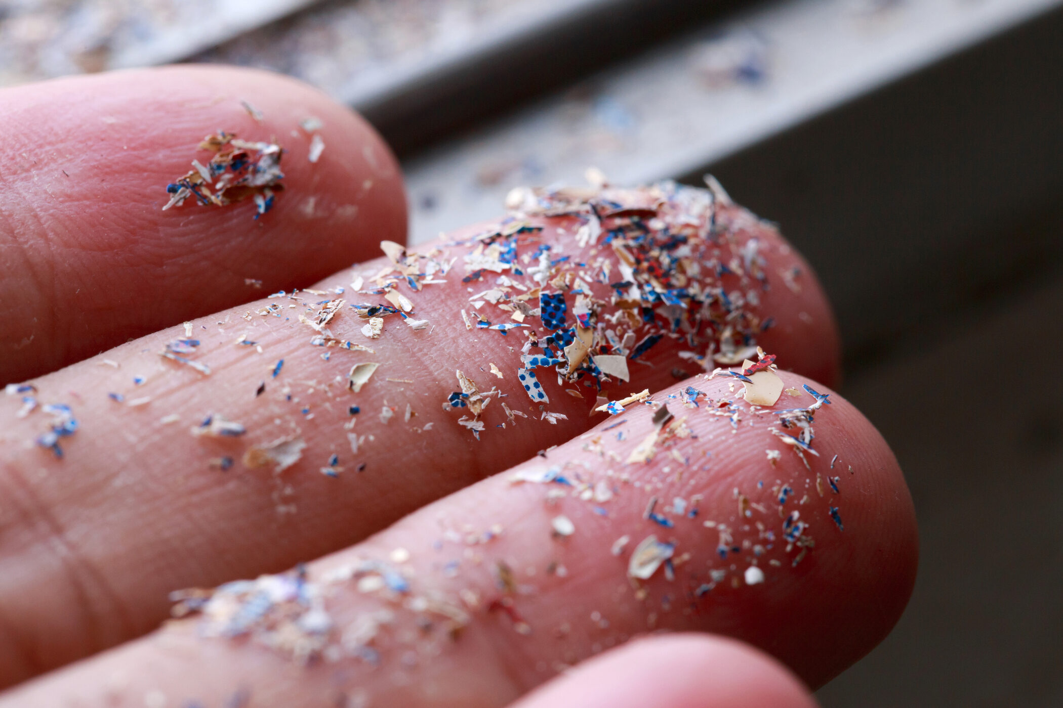 Tiny rainbow microplastic pieces on three fingers
