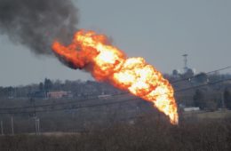 A massive tower of flames with black smoke as seen from afar