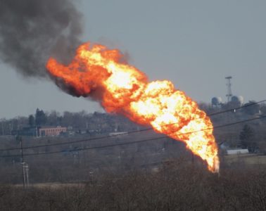 A massive tower of flames with black smoke as seen from afar