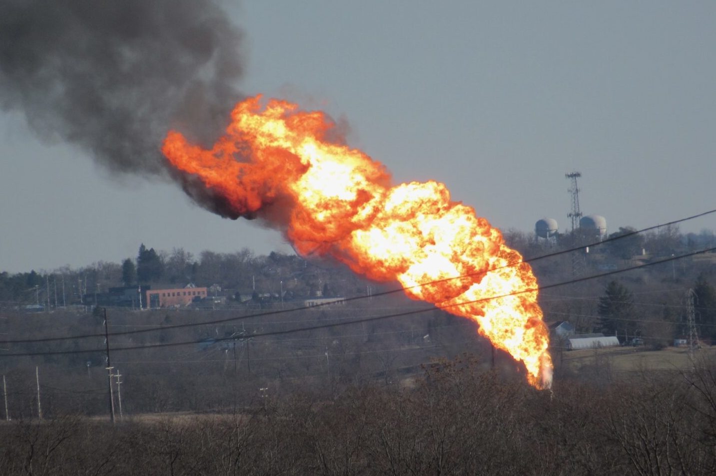 A massive tower of flames with black smoke as seen from afar