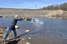 Senator Bob Casey throwing a bucket of trout into a lake