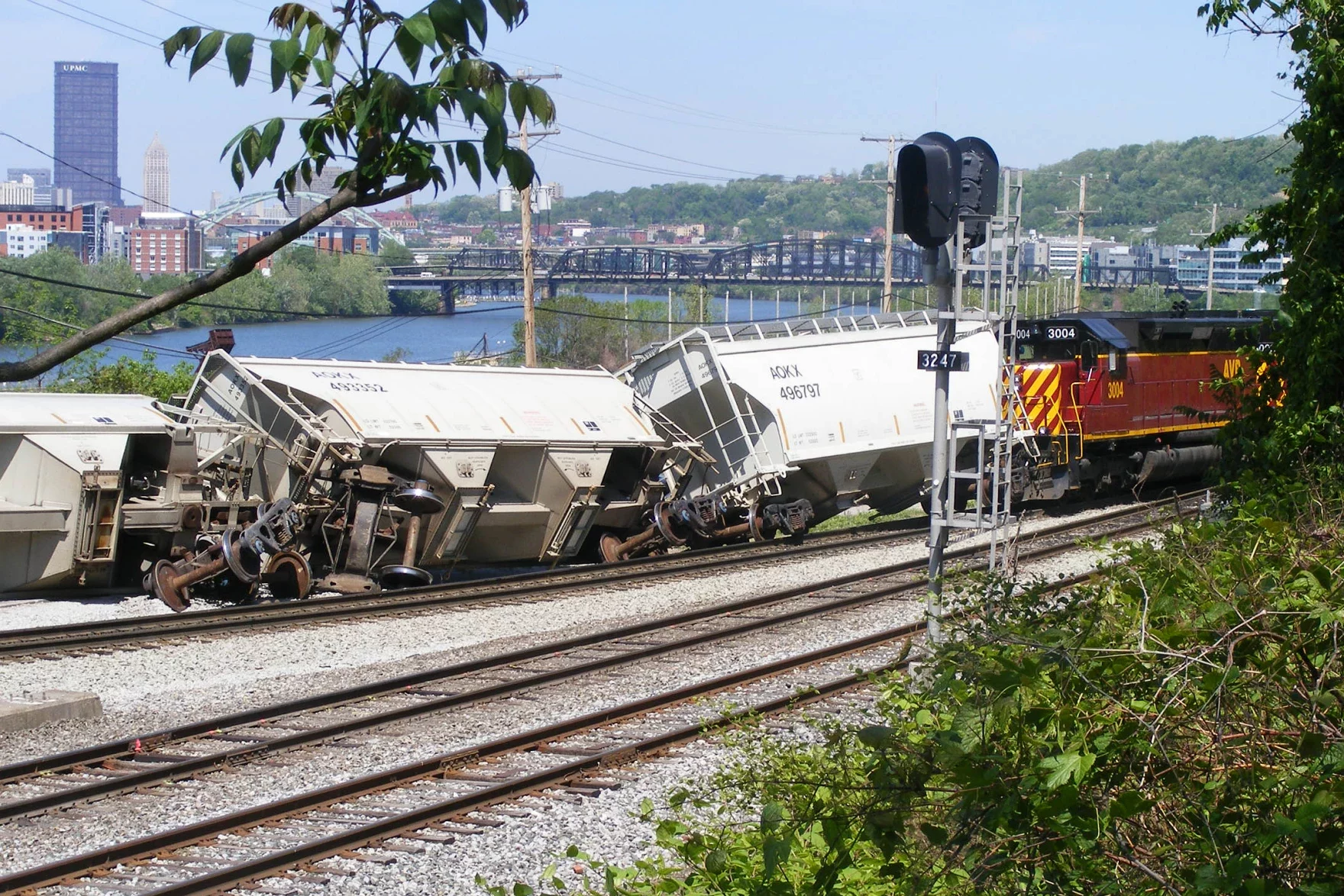 derailed train cars along tracks near Mon River with Downtown Pittsburgh in background