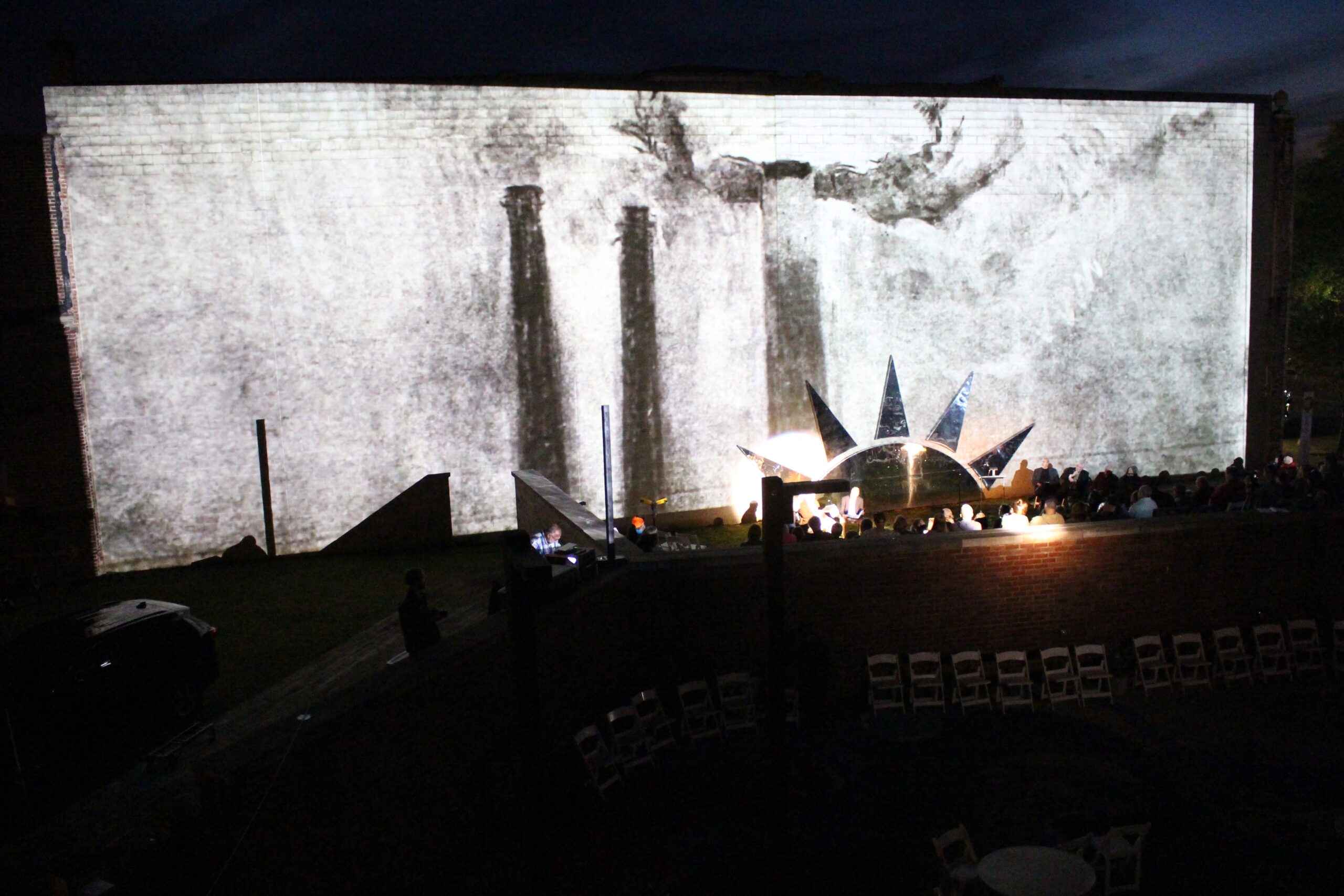 A black and white animation of smoke stacks is projected on a large brick wall above a stage