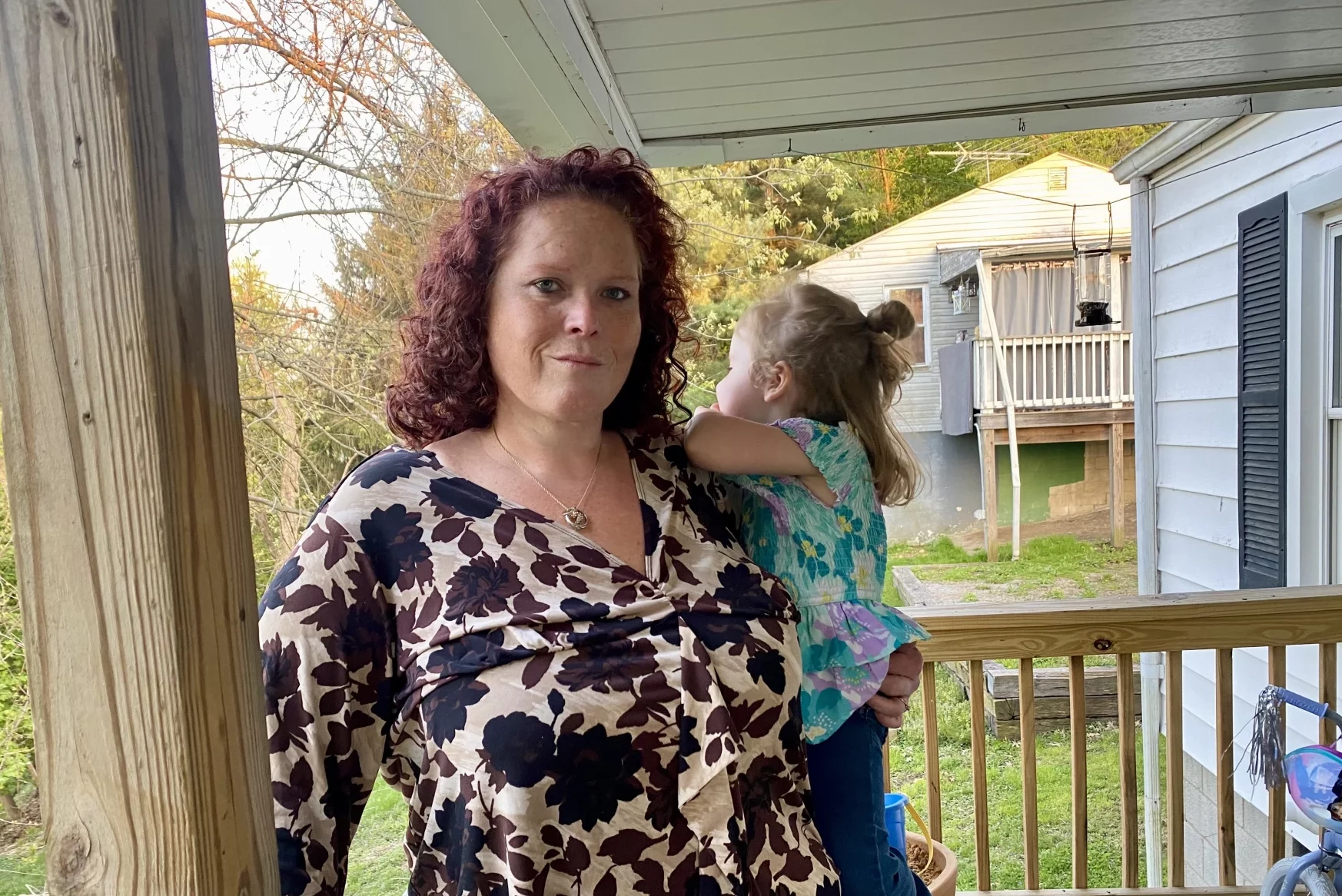 Kendall Crawford in a floral dress standing on a porch with her daughter