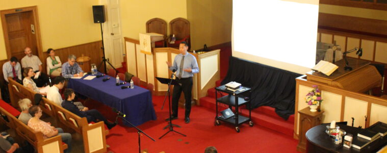 Dr. Arthur Chang in a church, speaking to a crowd