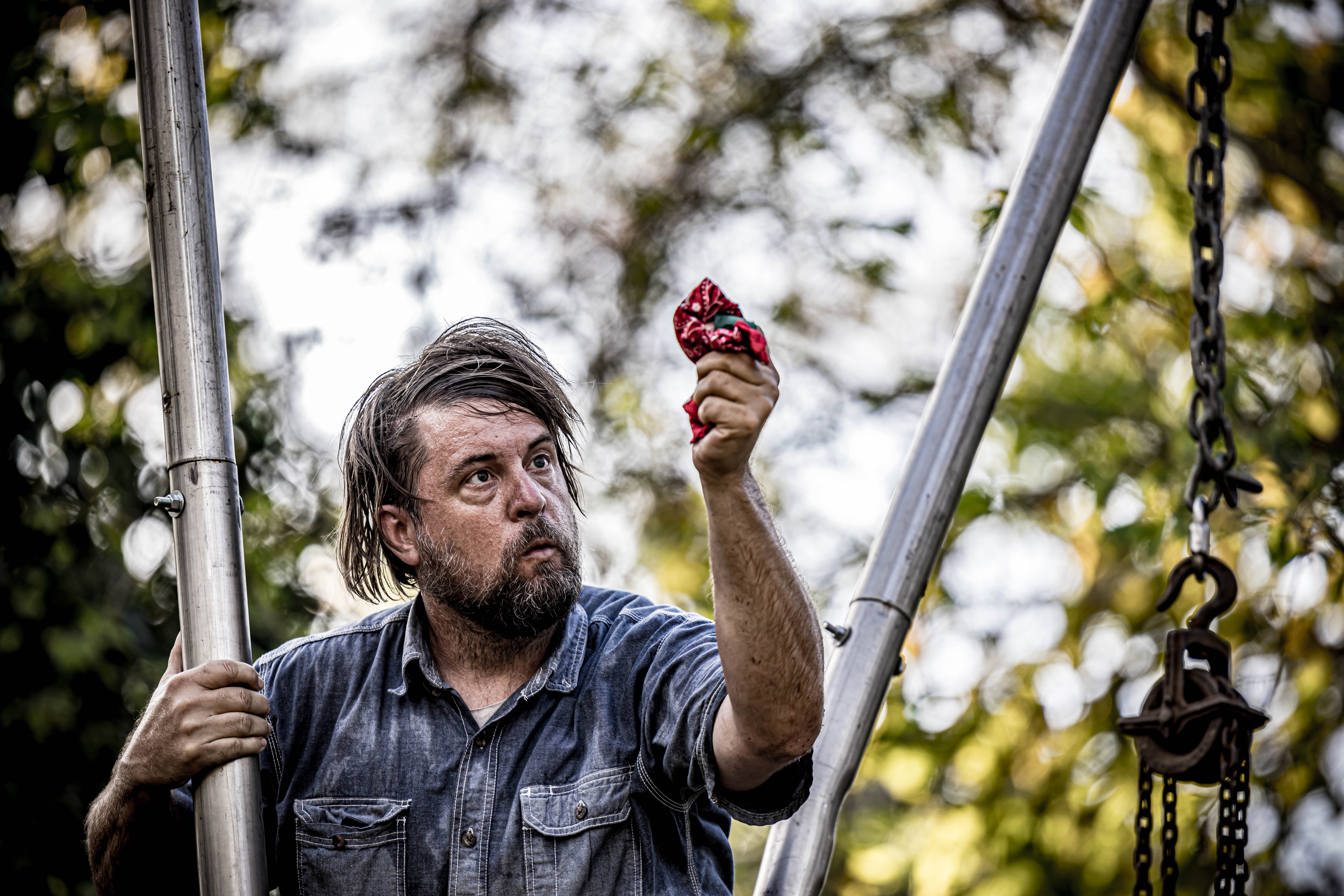 Actor Bob Martin portrays the character of Ezell, standing between two pipes and showin the audience a red hankercheif.