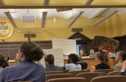 People with signs sitting at the county council meeting.