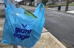 A blue Giant Eagle bag hanging on a fence post on a city street