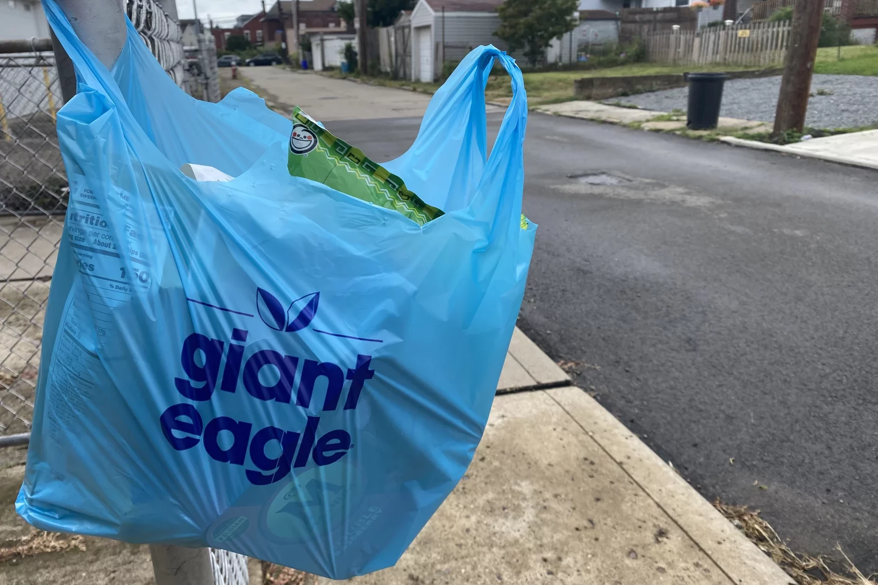 A blue Giant Eagle bag hanging on a fence post on a city street