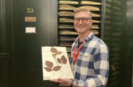 Mason Heberling in a plaid shirt holds up a sheet of paper with a dried poison ivy vine attached.