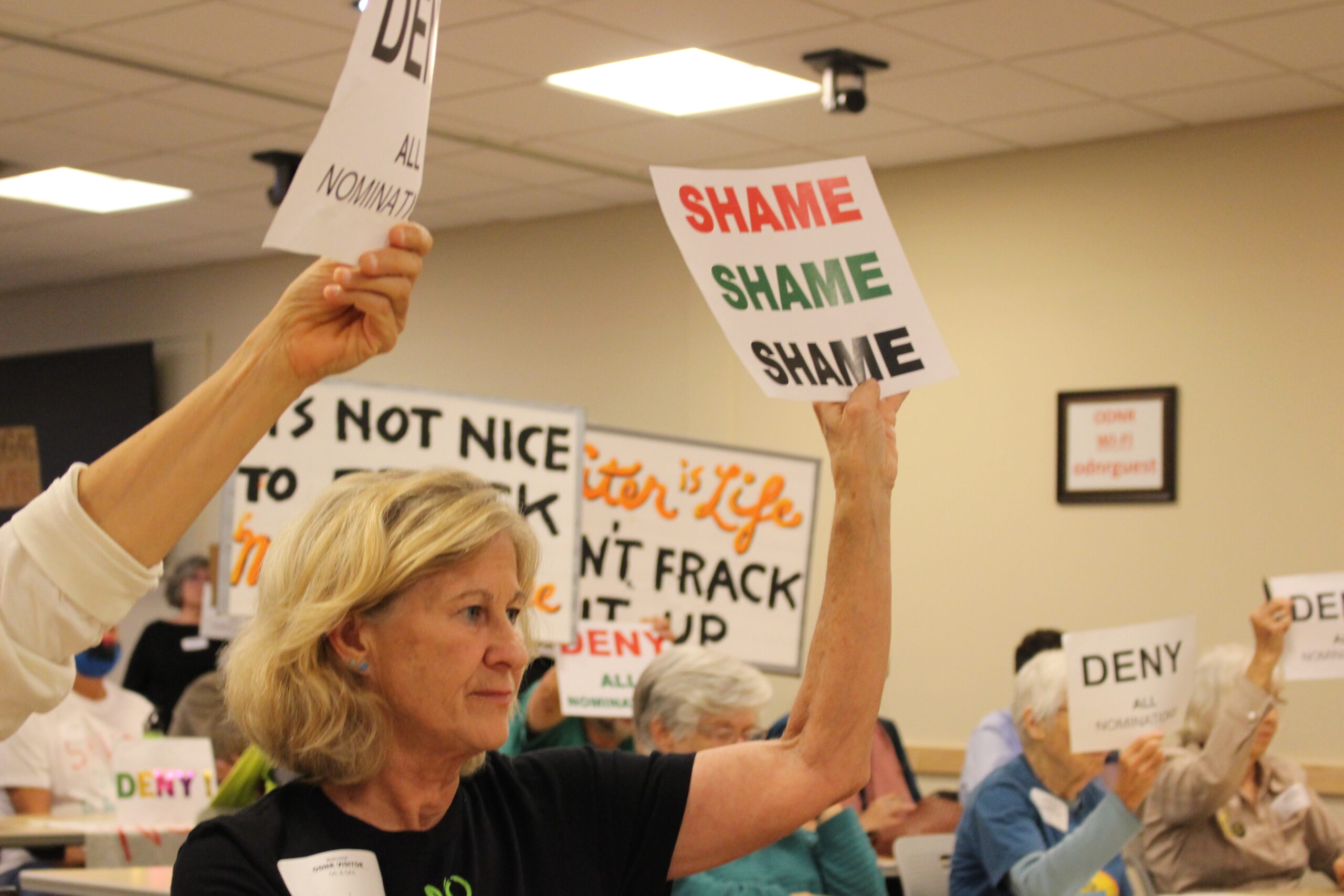 Woman holding a sign that says "SHAME, SHAME, SHAME" among other signs
