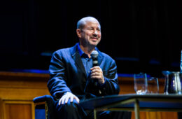 Michael Mann, a man in a blue suit, holds a microphone in front of an podium.