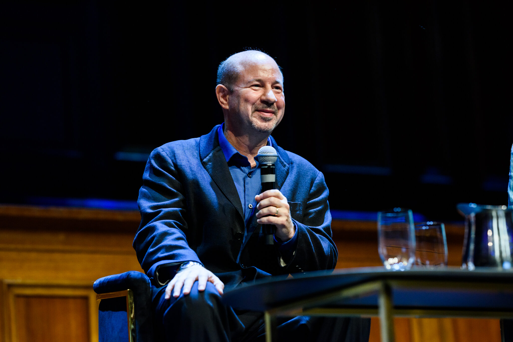 Michael Mann, a man in a blue suit, holds a microphone in front of an podium.