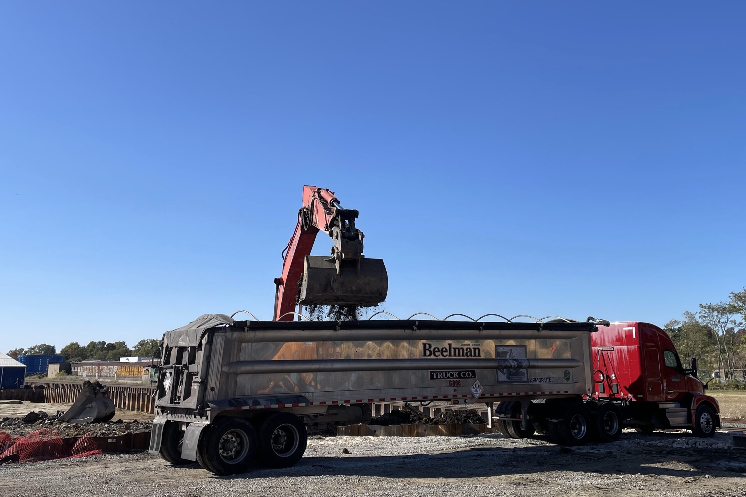 a front loader is dumping soil into a large tractor trailer truck in the foreground.