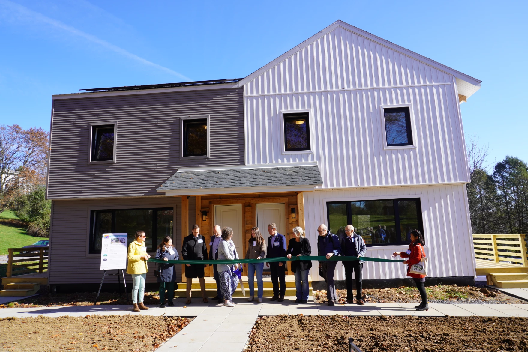 Eleven people state in front of a duplex holding a large ceremonial ribbon