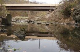 A stream with a rocky embankment with a concrete bridge over it