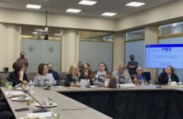 Seven adults and a child sit at an L-shaped conference table