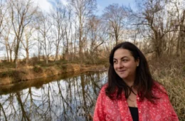 A woman with a red blouse stands near a stream