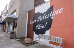 The brick facade of a store is painted with the words "East Palestine, Ohio" in red white and blue.