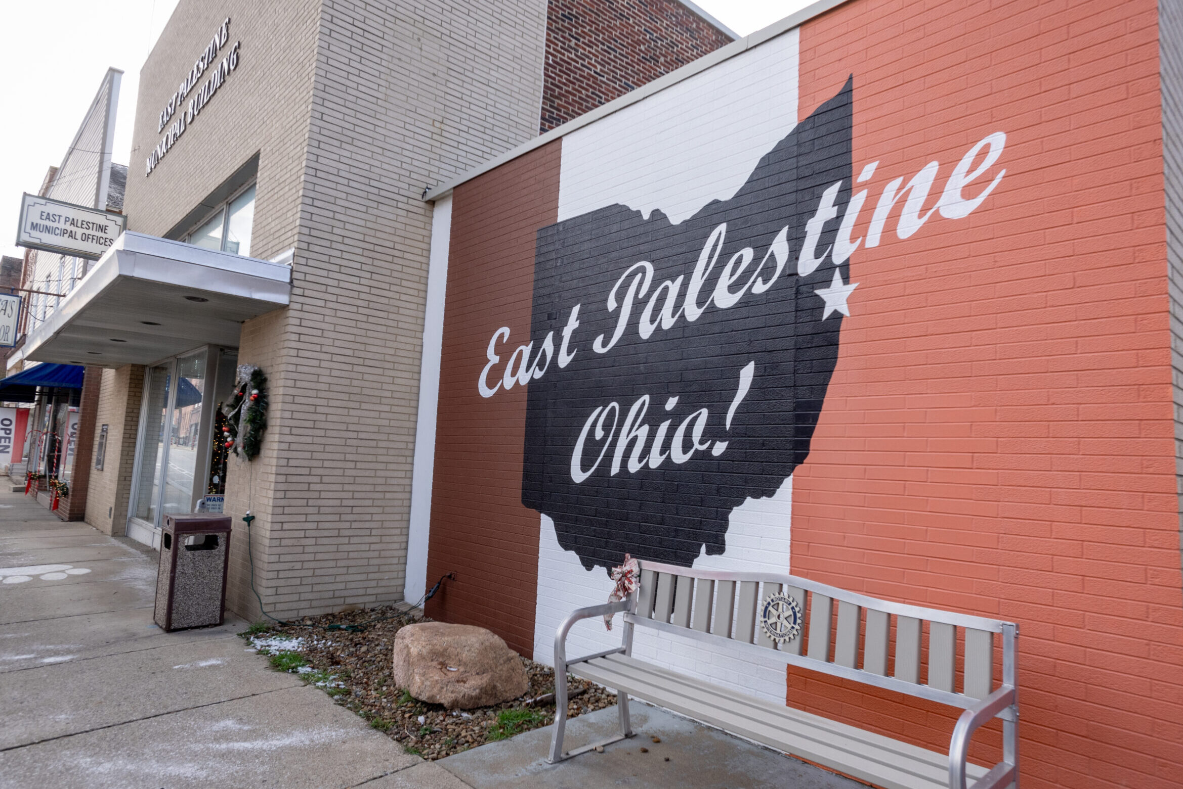 The brick facade of a store is painted with the words "East Palestine, Ohio" in red white and blue.