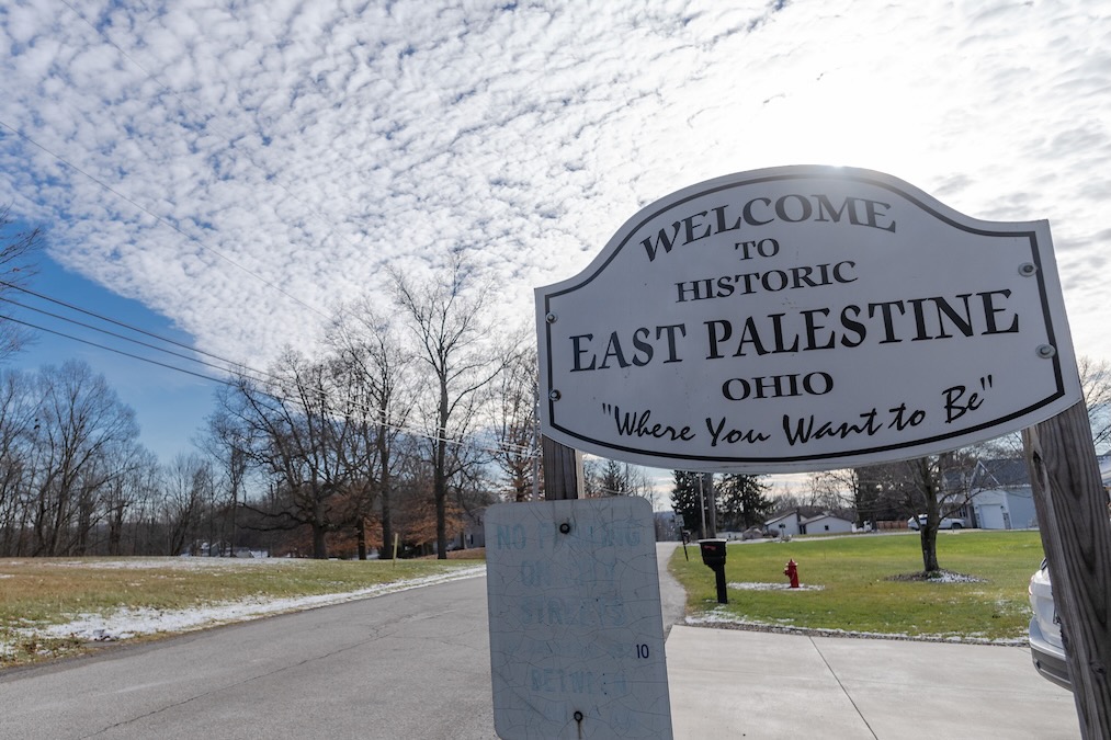 A sign reading "Welcome to East Palestine, Oho, Where you want to be" along a road