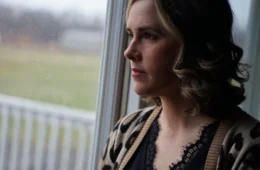 A woman looks about the window of her home