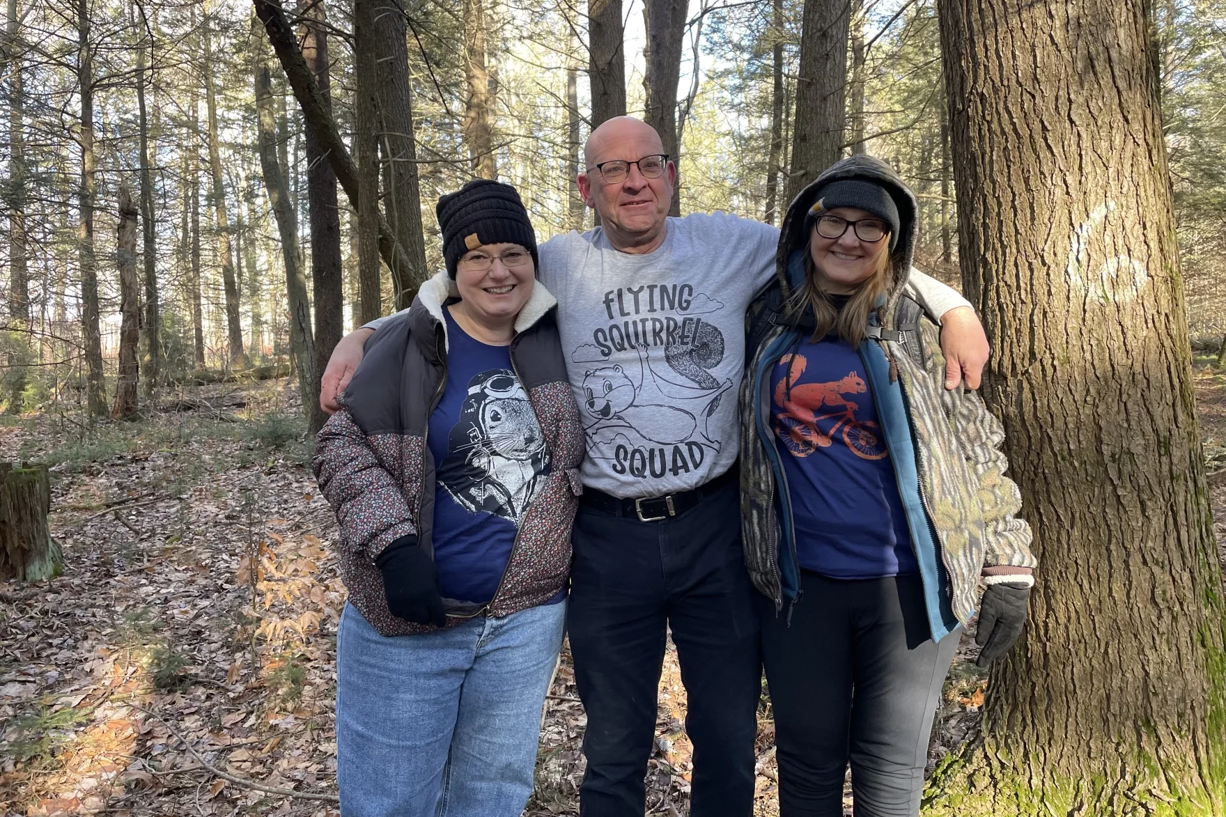 Three people stand arm-and-arm in a forest.
