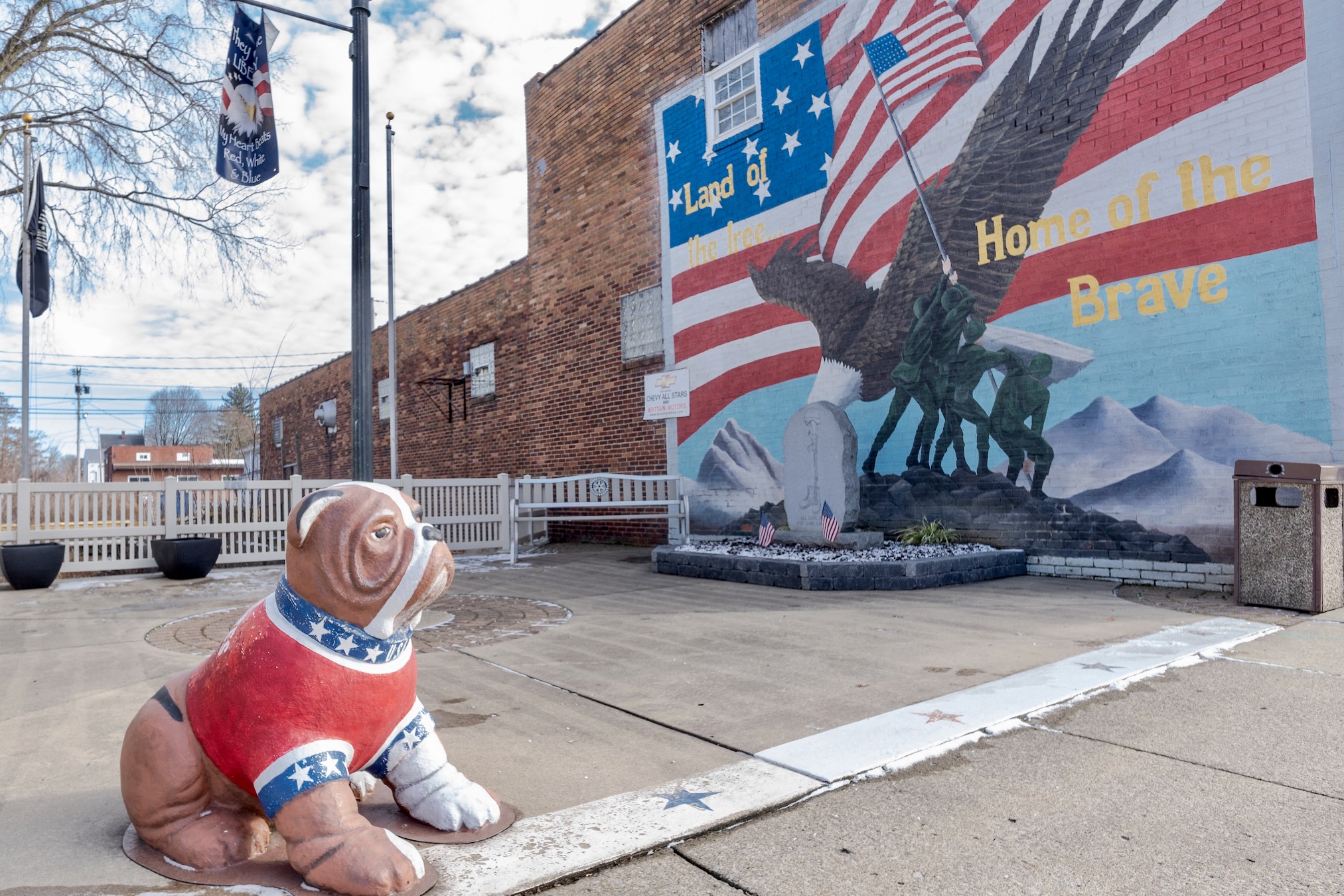 A statue of a bulldog painted red, white and blue sits along the sidewalk with a patriotic mural in the background