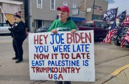 Don Skowron, wearing a red MAGA hat, stands on the street with a sign that reads, "Hey Joe Biden. You were late. Now it's too late. East Palestine is Trump country U.S.A.," in Downtown East Palestine.