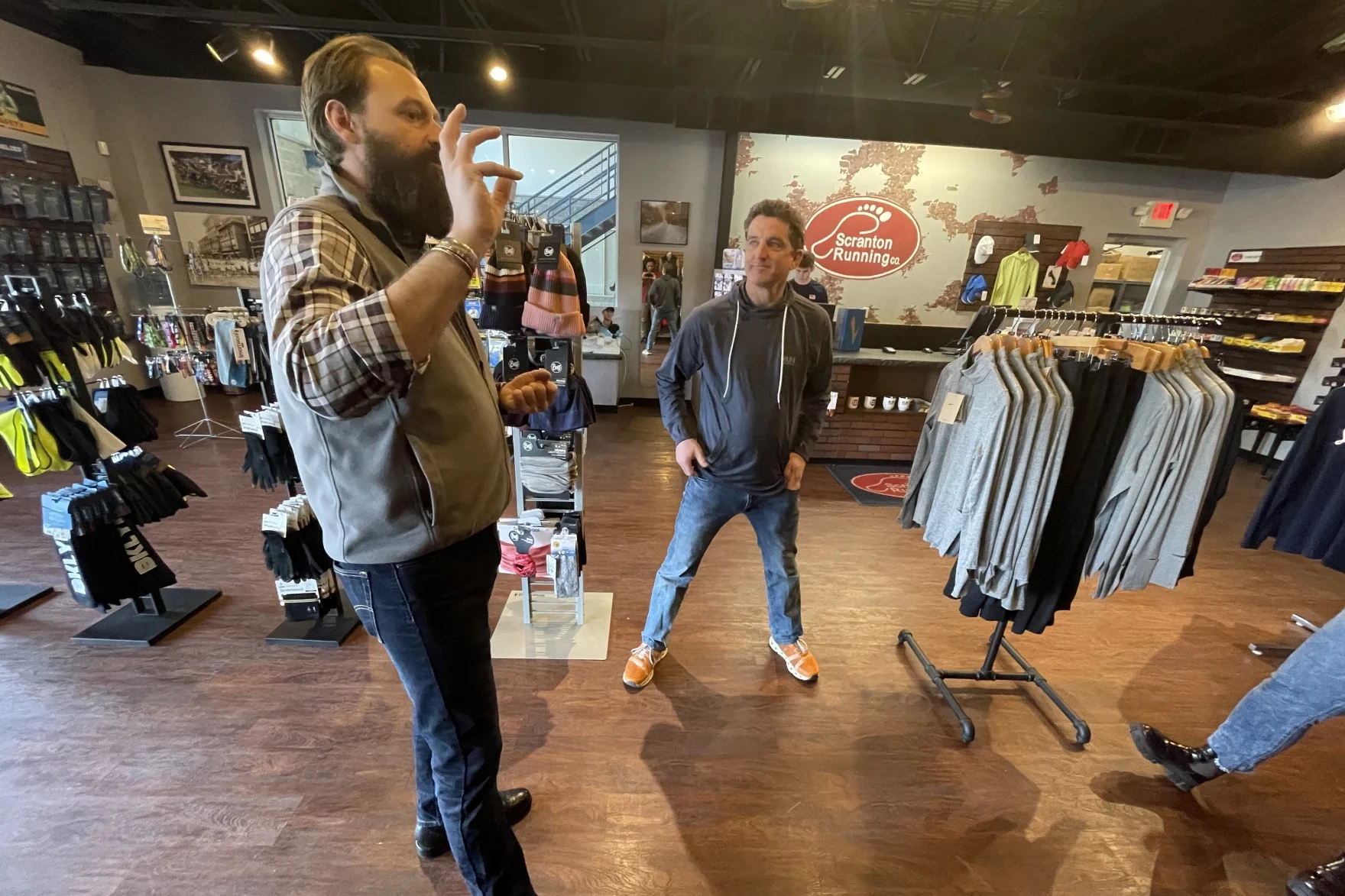 Two men stand inside a store with clothing and other outdoor gear.
