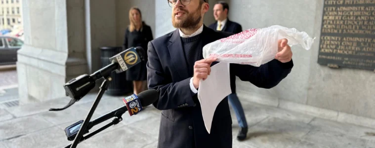 A man holds a plastic bag as he talks in a microphone outside a buidling