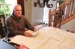 A man sits at a dining room table with a large document showing property lots