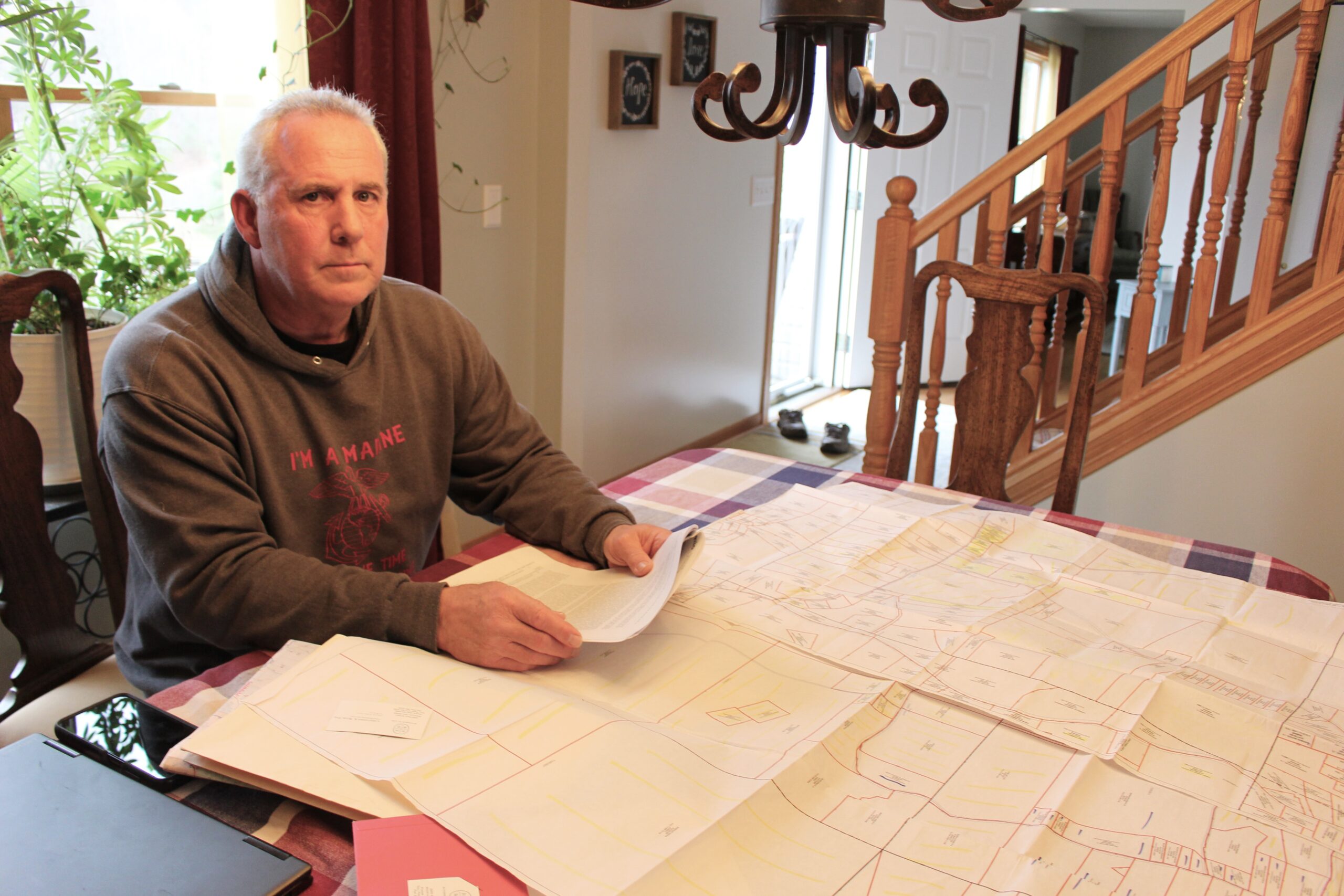 A man sits at a dining room table with a large document showing property lots