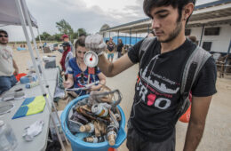 A man holds a blue bucket filled with cans, bottle and other trash picked up at beach clean up.