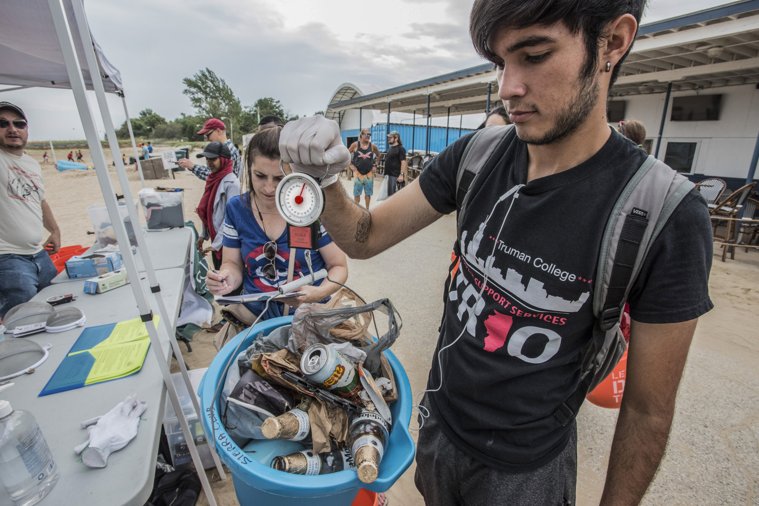 A man holds a blue bucket filled with cans, bottle and other trash picked up at beach clean up.