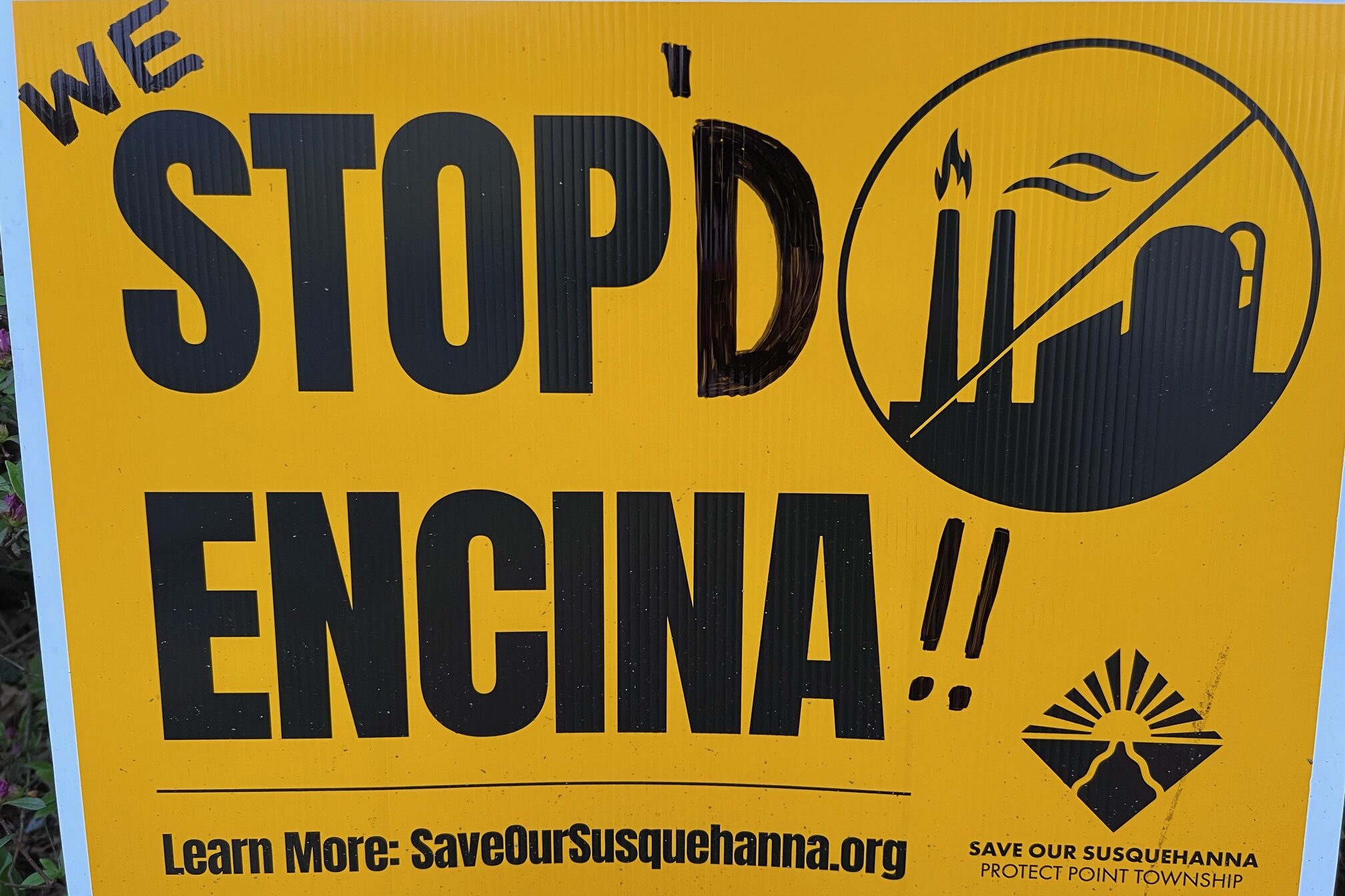 A tellow sign with bold, black lettering against the Encina plant in Point Township.