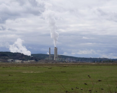 A power plant with large smokestacks shown from a distance.