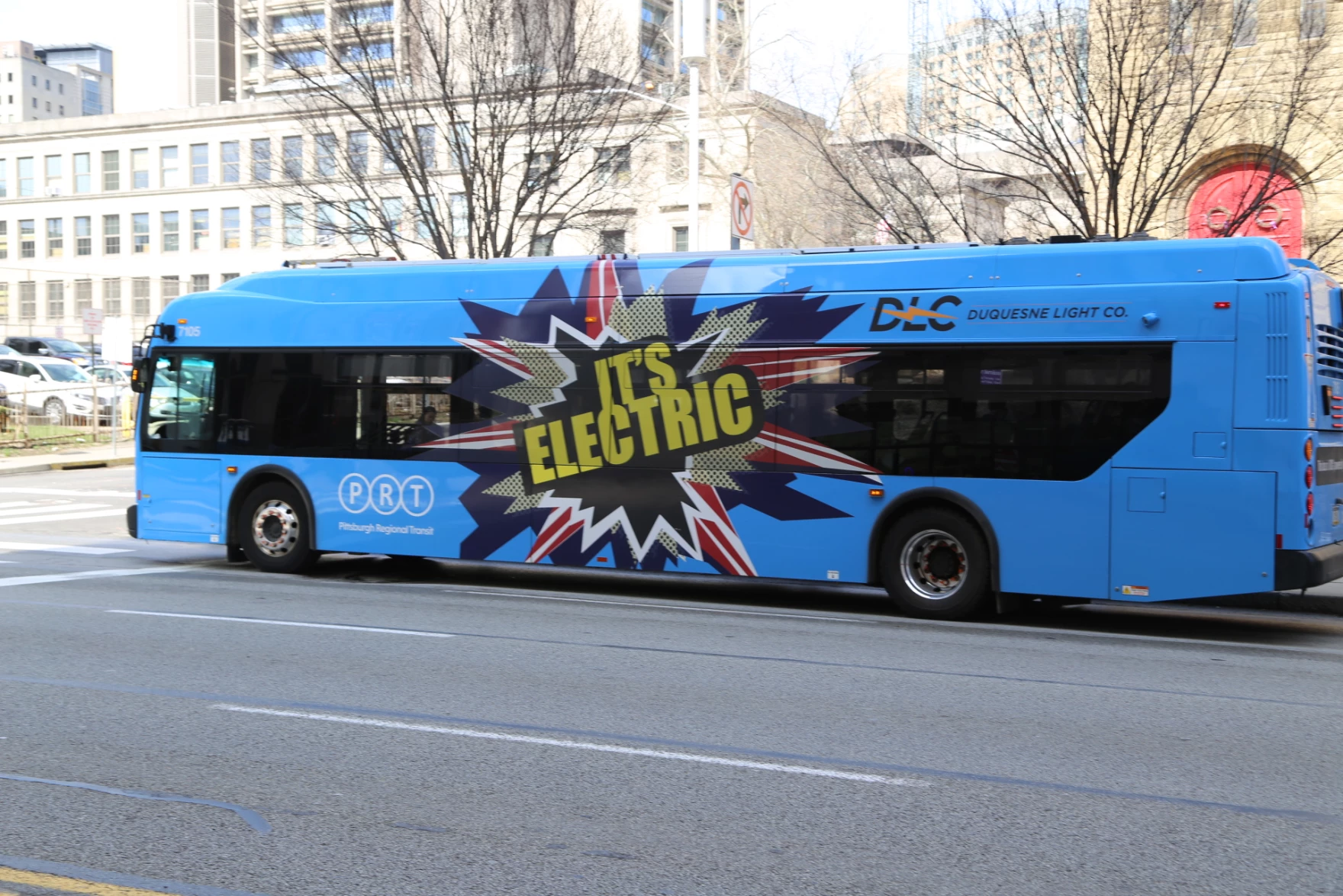 A blue city bus with words in yellow that say "It's Electric."