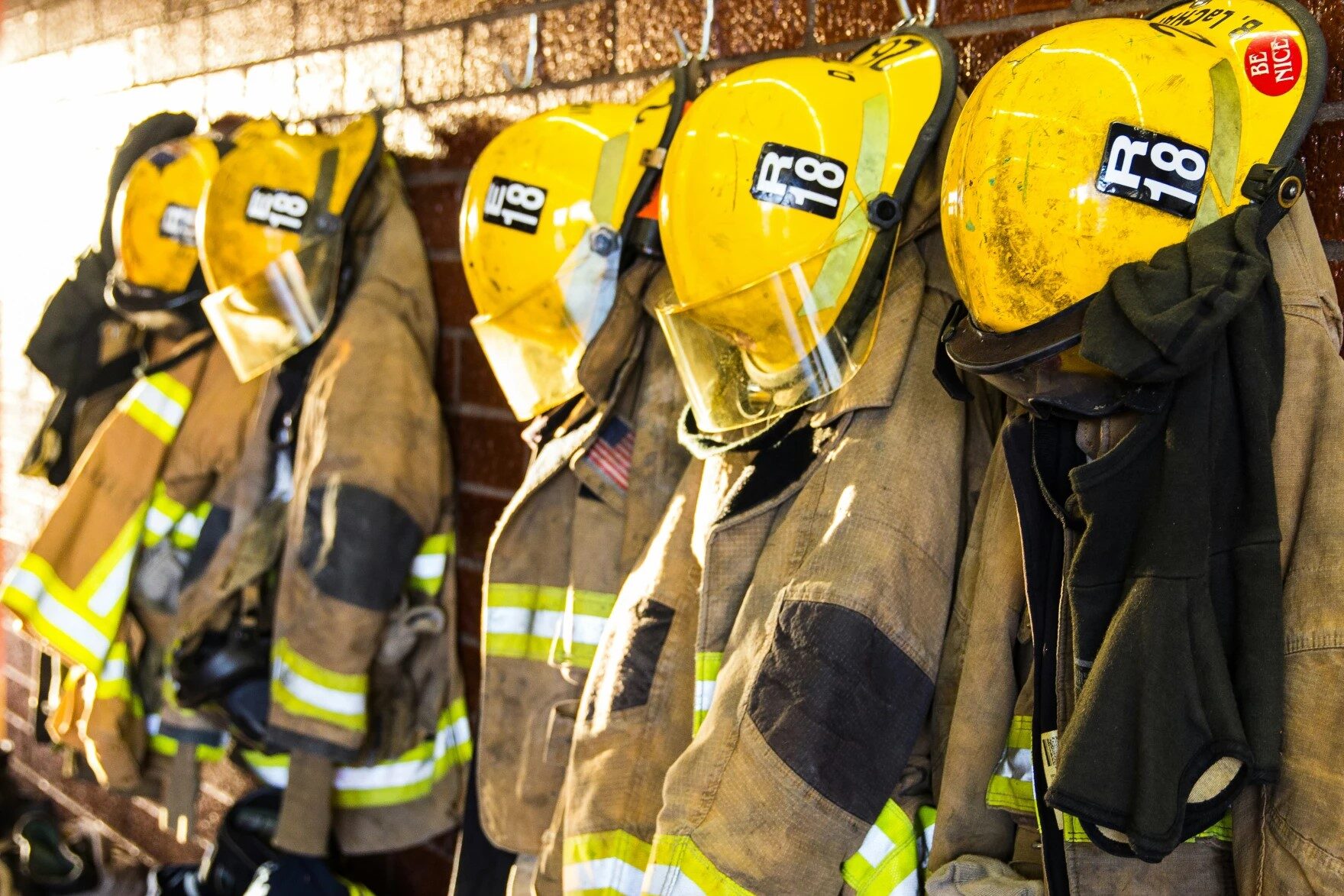 A row of beige fireflighter jackets and yellow hats hanging on hooks