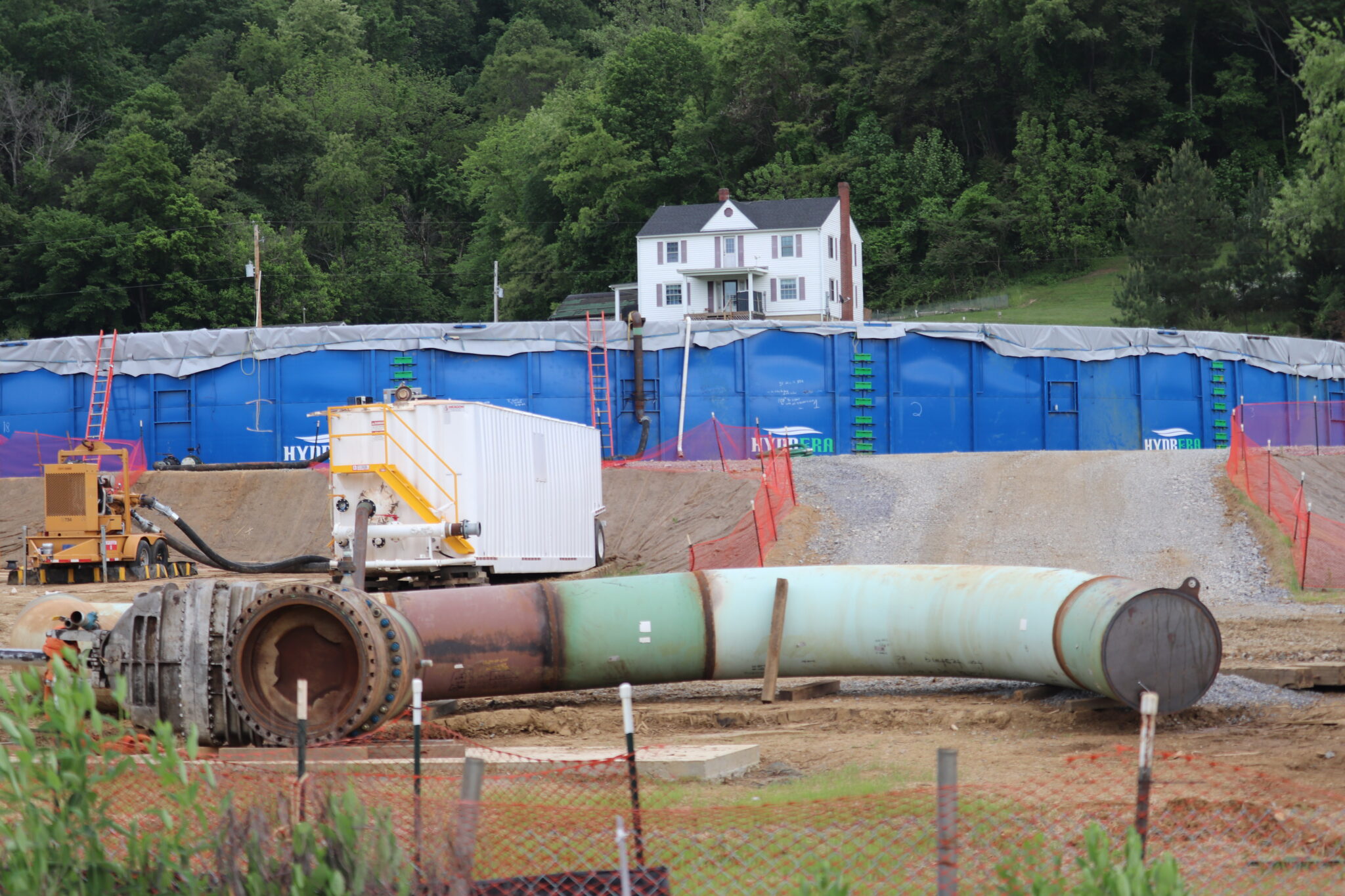 A section of pipeline and other construction equipment in front of a house that sits in the background.