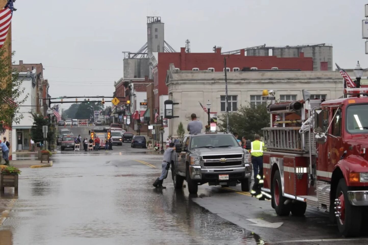 A downtown street is flooded with water and a silver truck is parked on a sidewalk