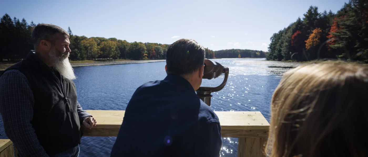 A person looks through a viewfinder overlooking a lake.