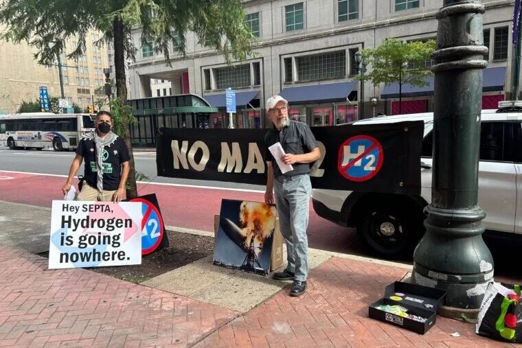 Two men with protest signs stand on the side of the street