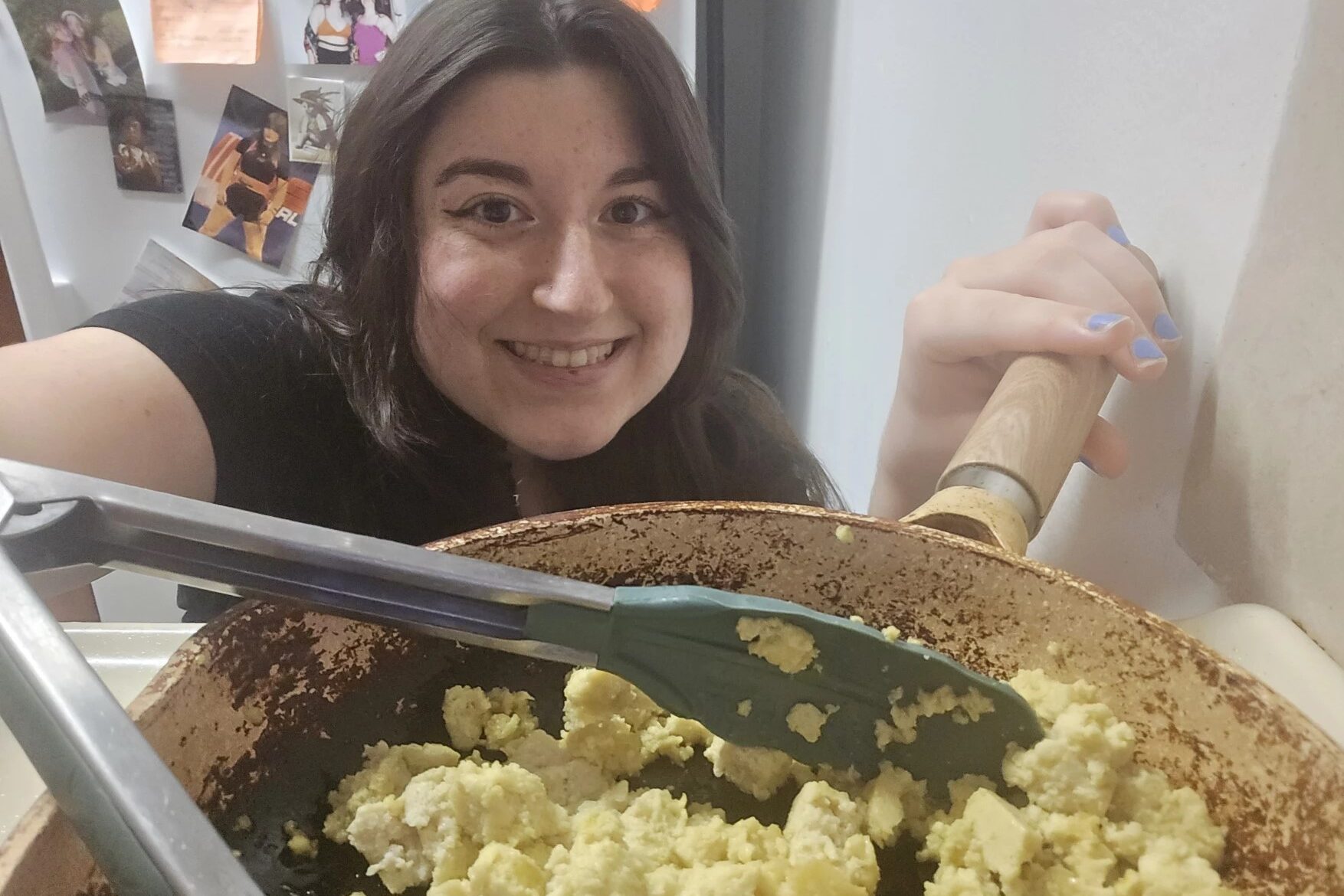 A woman in black shirt holds up a frying pan of tofu and tongs