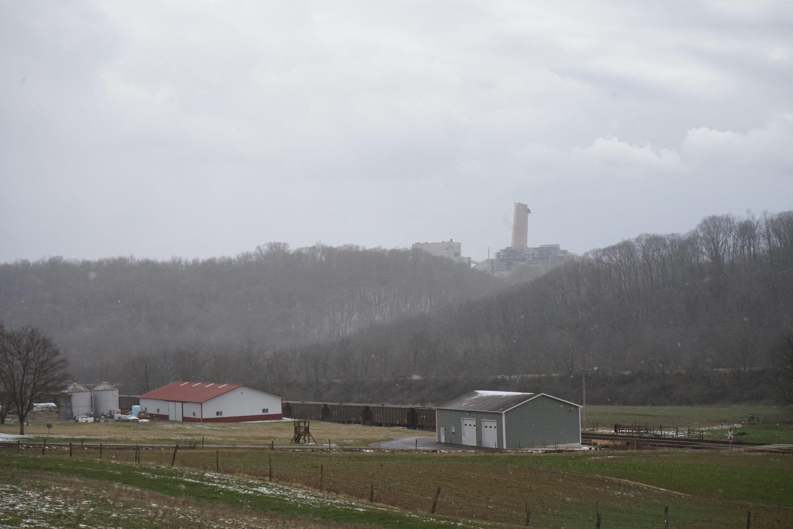 A farm sits below a hill with a stack in the background
